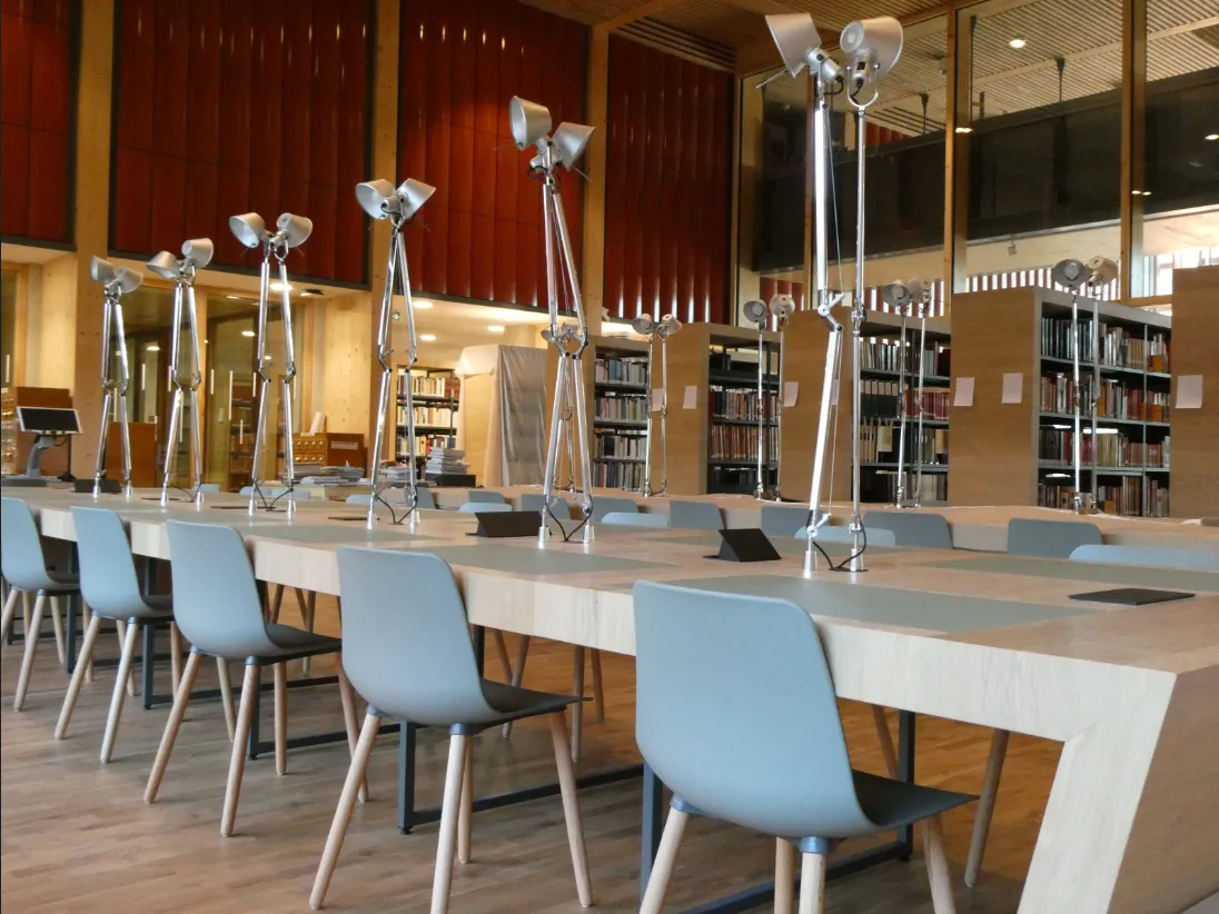 Vue sur une grande salle de consultation récente, dotée de bibliothèques, de grandes tables de consultation en  bois avec lampes orientables