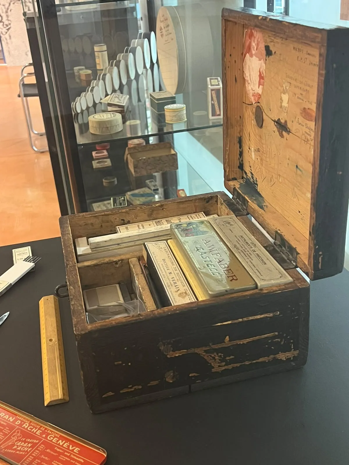 Vue sur le côté droit d'un coffret bois contenant divers ustensiles rangés dans des compartiments, une photo figure à l'intérieur du couvercle dans le coin en haut à gauche
