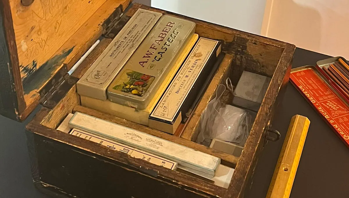 Vue sur le dessus d'un coffret bois contenant divers ustensiles rangés dans des compartiments.