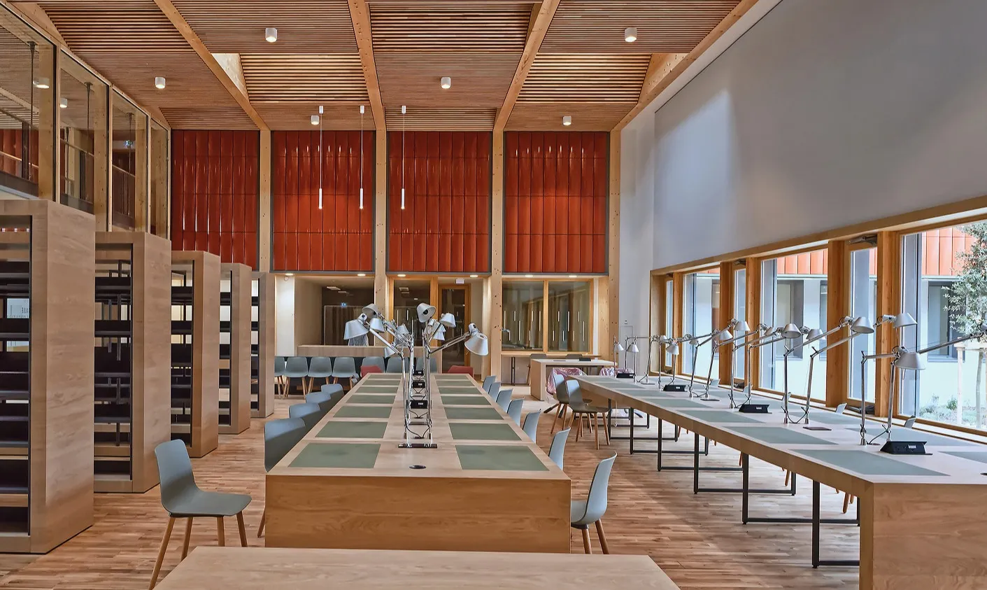 Vue sur une grande salle de consultation récente, dotée de bibliothèques, de grandes tables de consultation en  bois avec lampes orientables et de baies vitrées