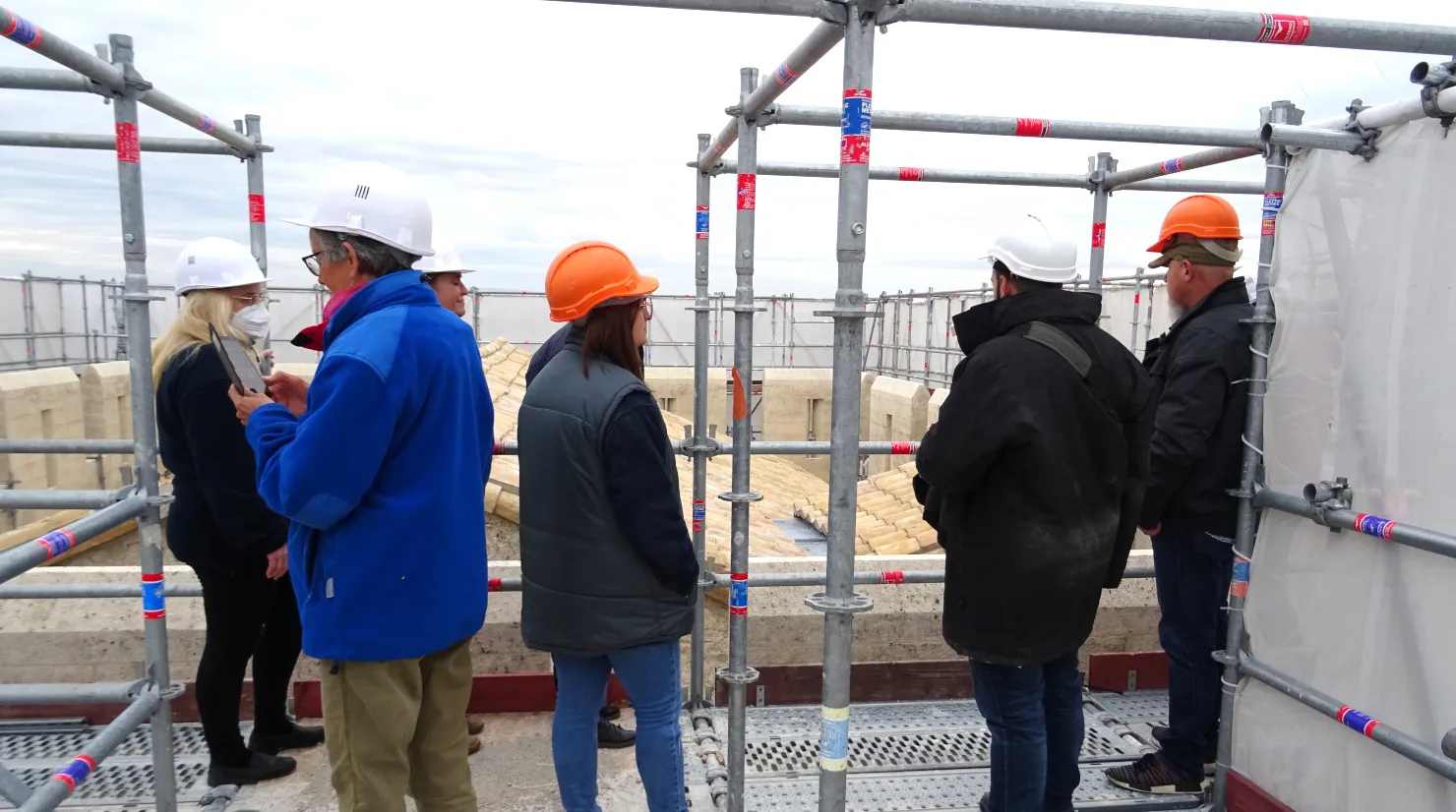 Groupe de personnes coiffées de casques de chantier sur un échafaudage dominant une ville