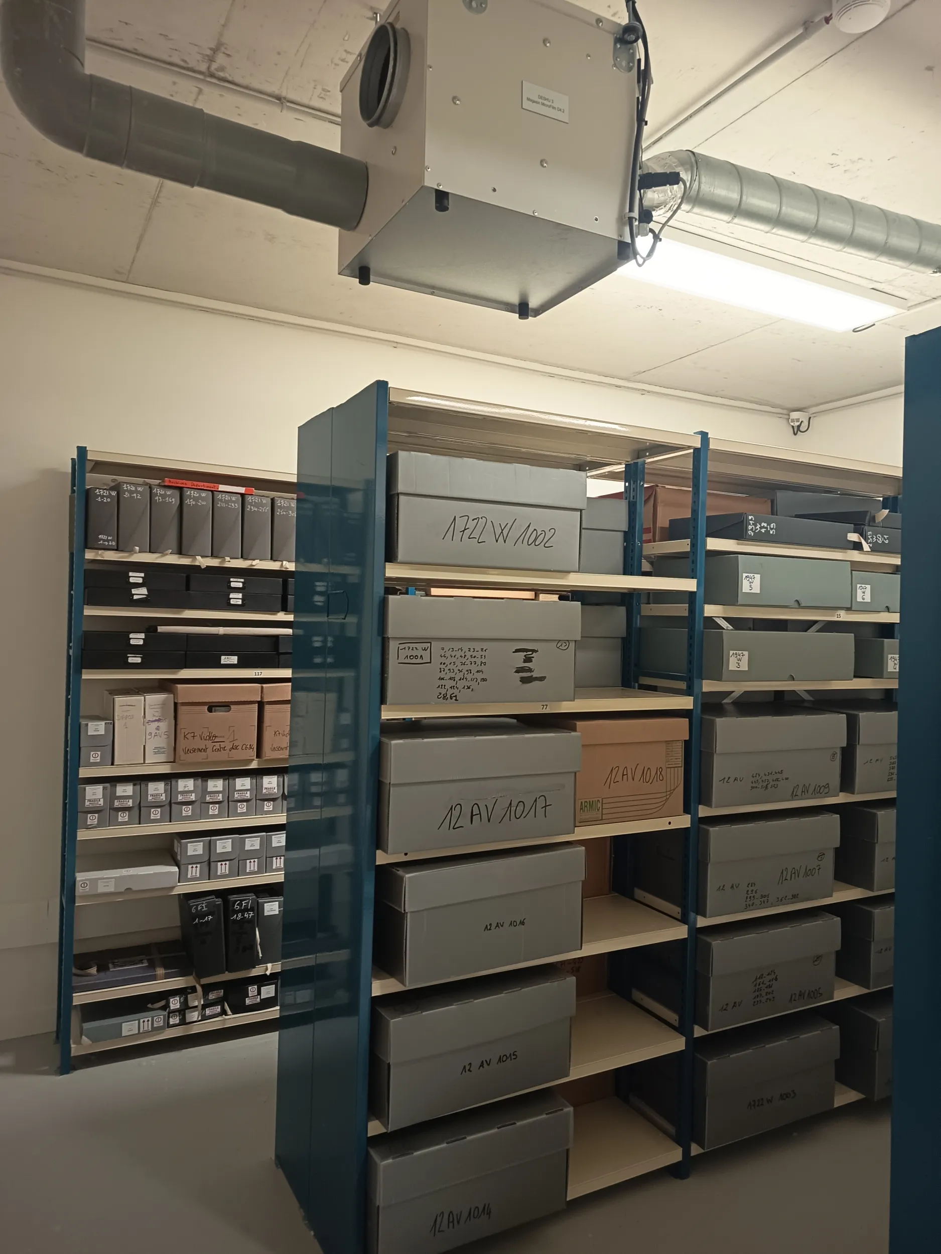 Espace clos éclairé de néons, des boîtes cartonnées reposent sur des rayonnages métalliques