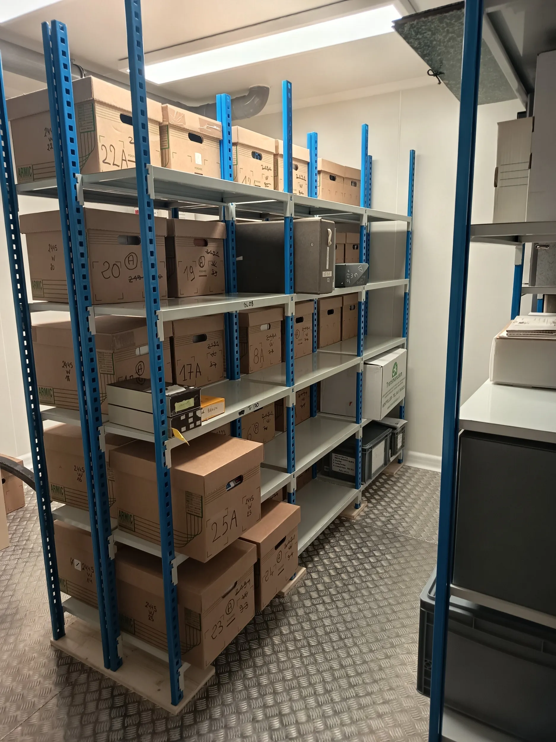 Espace clos éclairé de néons, des boîtes cartonnées reposent sur des rayonnages métalliques