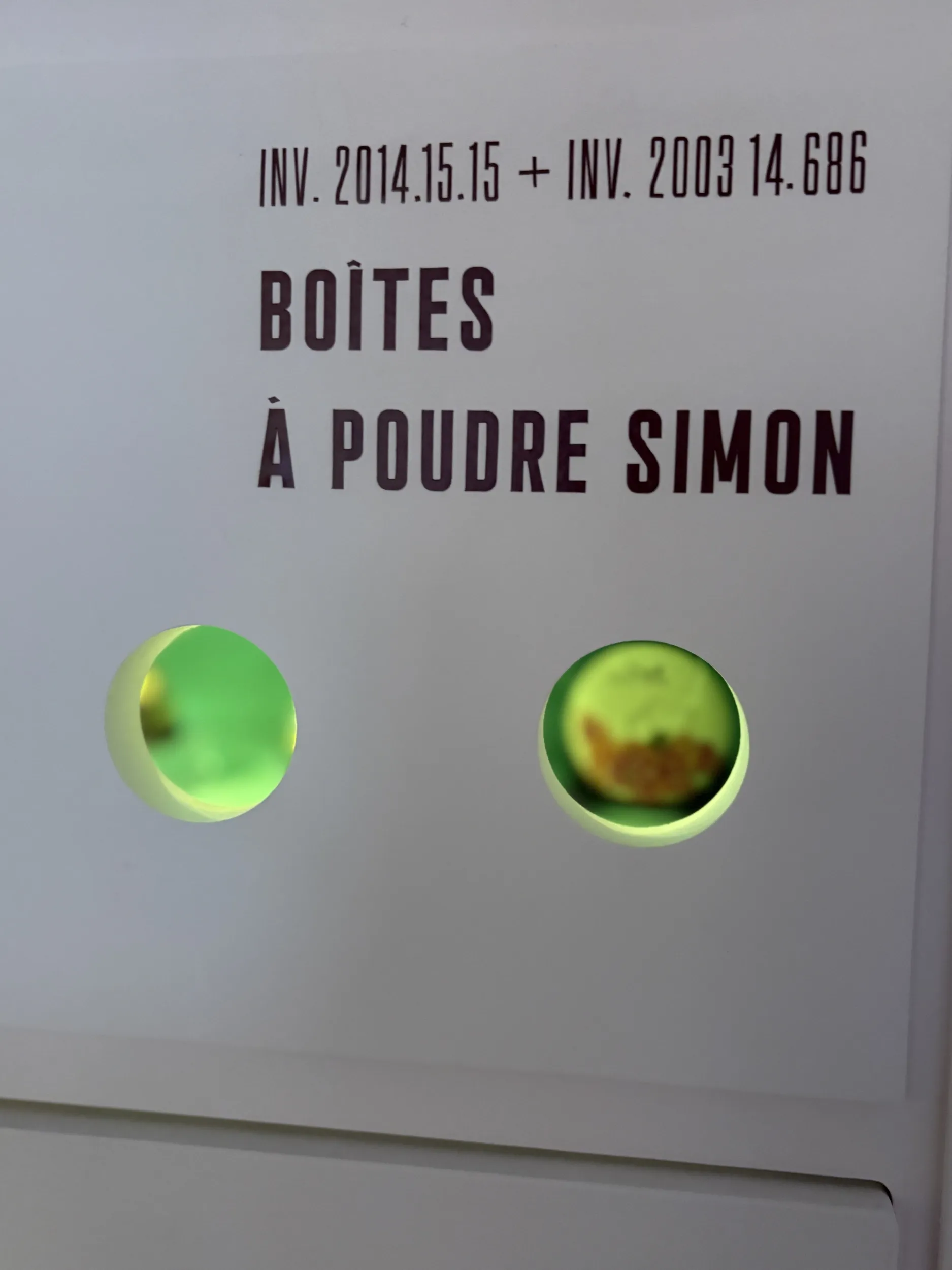 Vue sur une cloison portant la mention "Boîtes à poudre Simon" dotée de 2 oculus éclairés derrière lesquels figurent des objets