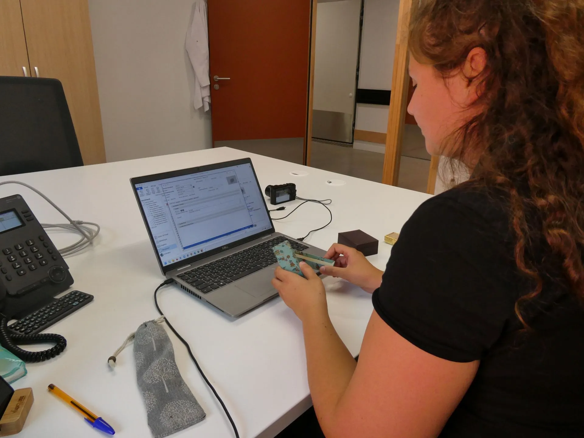 Un agent devant un ordinateur portable tient en main une boîte qu'elle s'apprête à décrire informatiquement.