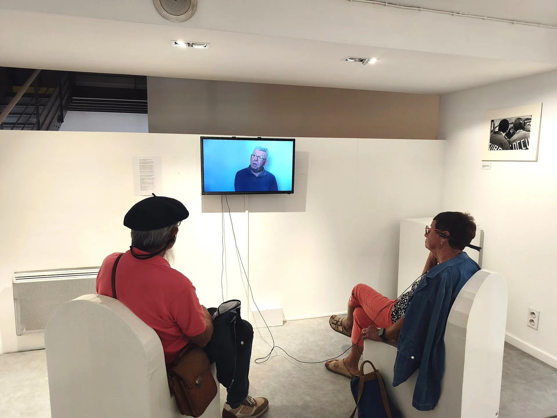 Un homme et femme équipés de casque audio, regardent un film sur un écran fixé au mur.
