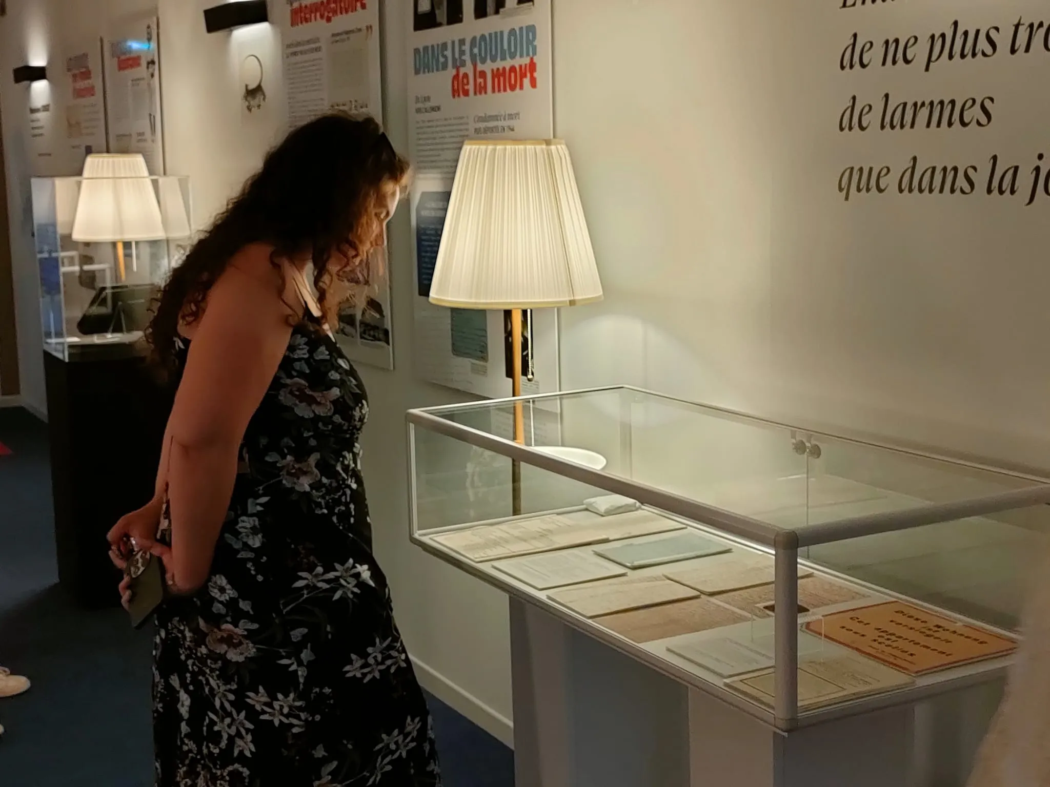 Une visiteuse contemple une vitrine éclairée d'une lampe sur pied, dans laquelle des documents sont exposés