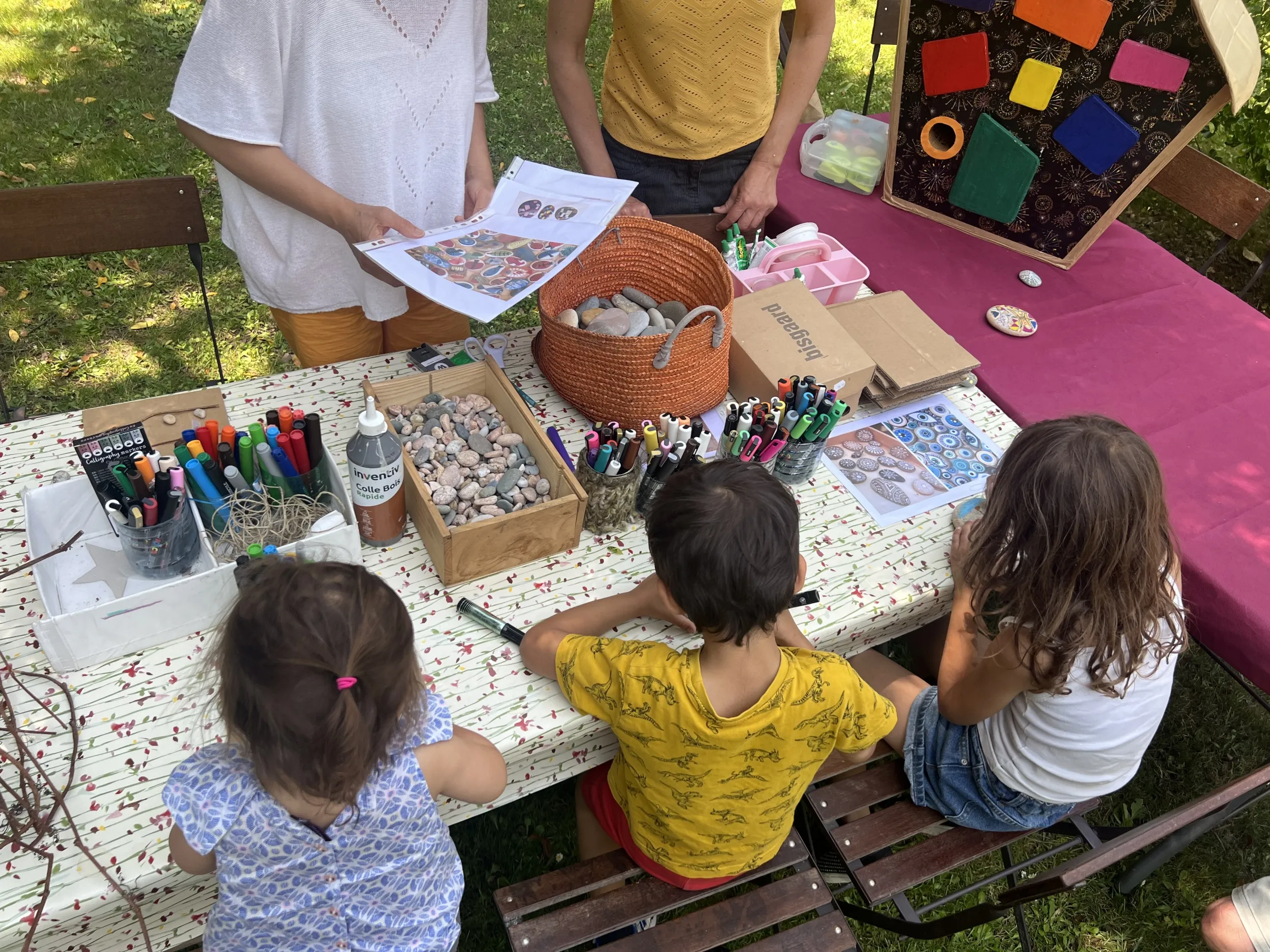 Trois enfants de dos, attablés dessinent ; en face, des médiateurs les accompagnent