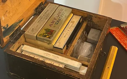 Vue sur le dessus d'un coffret bois contenant divers ustensiles rangés dans des compartiments.