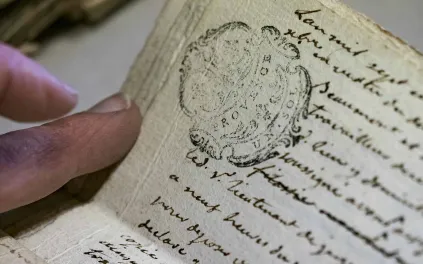 Une main tient un vieux texte manuscrit sur lequel figure un timbre et la mention "Provence, Un sol"