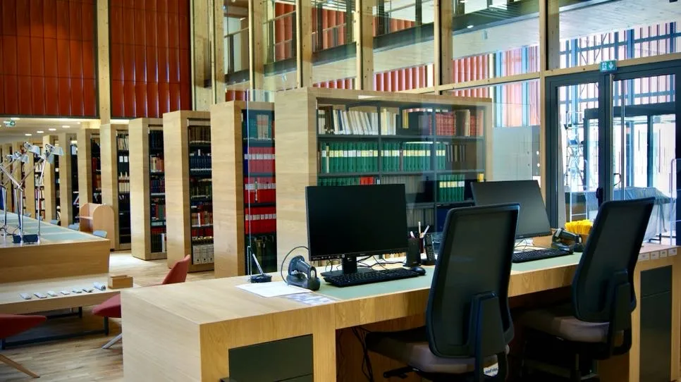 Vue en profondeur sur une salle de consultation depuis une banque d'accueil ; à droite, une bibliothèque