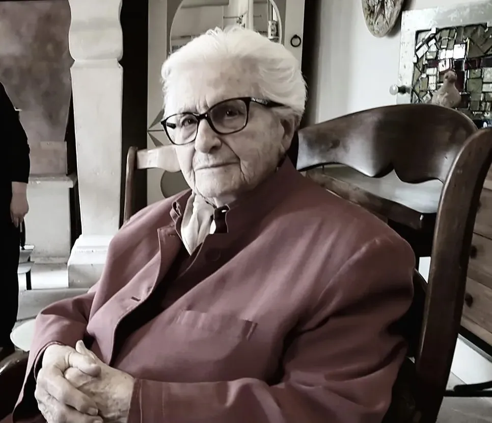 Portrait en buste d'une dame âgée, cheveux courts blancs, lunettes et veste rose poudrée.